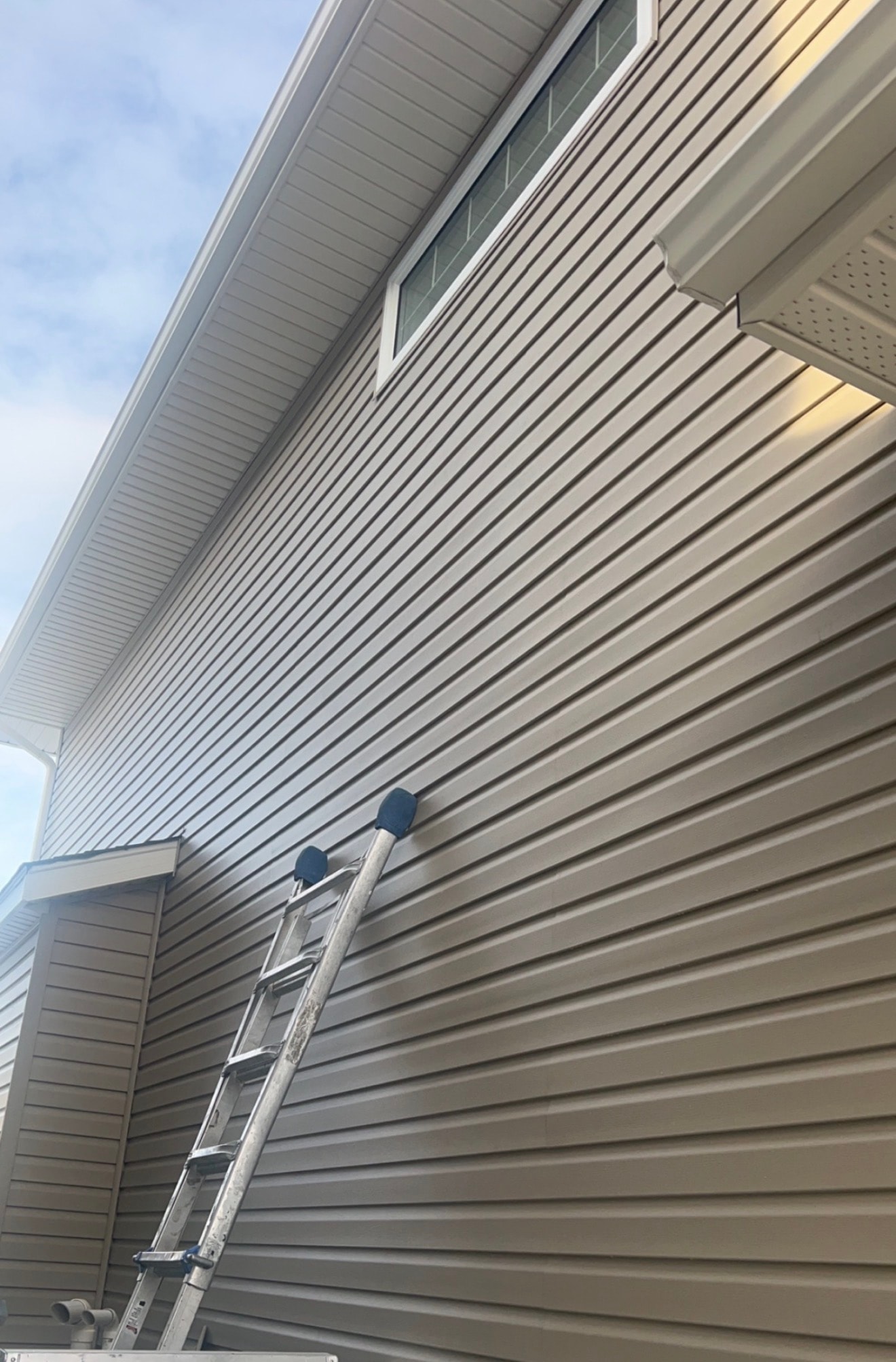 Taupe vinyl siding with white soffit and fascia, ladder on site — BWK Exteriors Regina